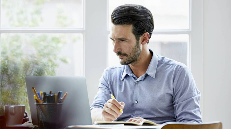 Man with beard sitting at desk with laptop and pen