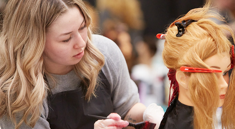 A hairstyling student applying dye to a mannequin